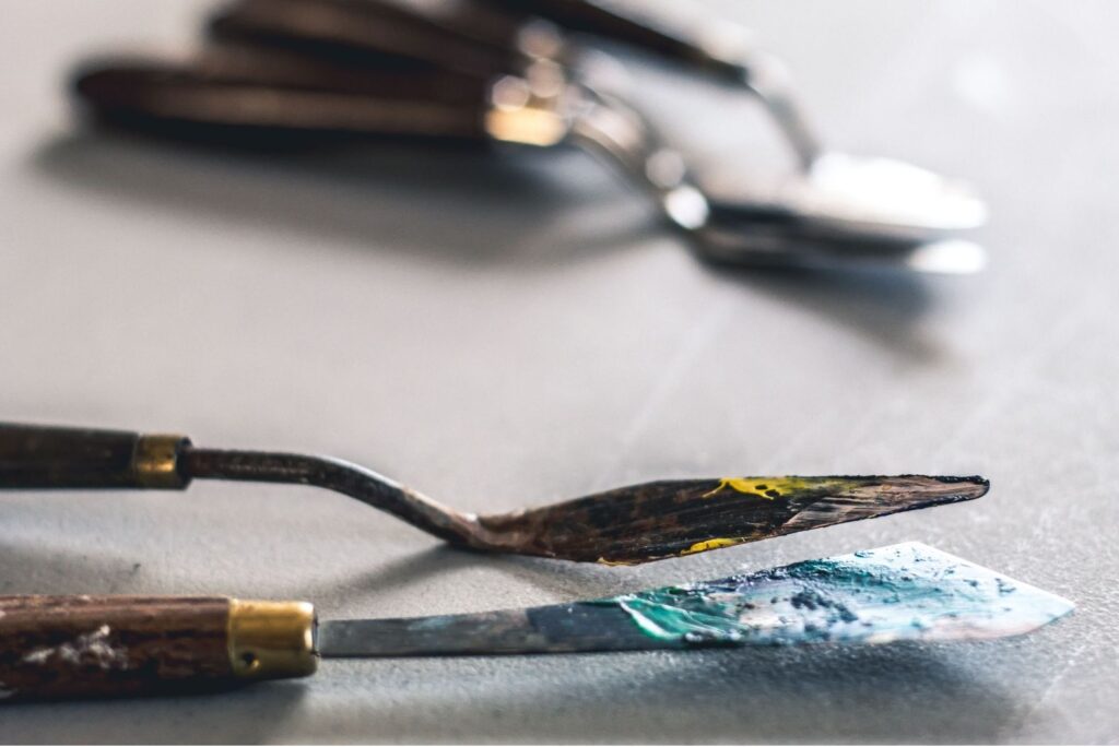 Two palette knives with dried paint on their blades, resting on a work surface