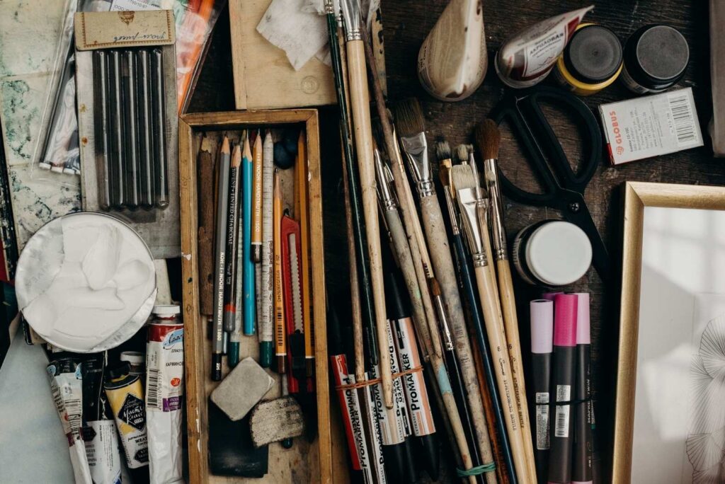 An artist's desk with pencils, brushes, paint tubes, and other art supplies laid out