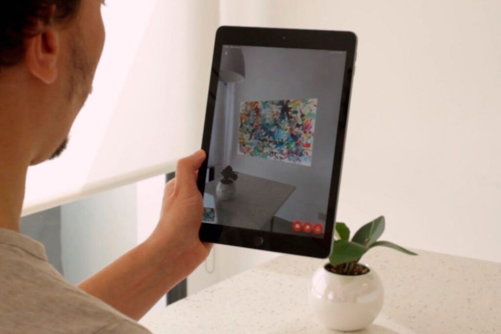 Person using an augmented reality art app to preview a painting on a their real wall via tablet camera.