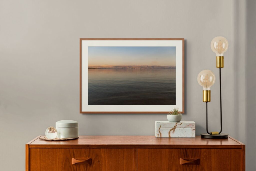 Framed seascape photograph above a wooden sideboard with brass lamps, shown in an ArtPlacer Room Mockup.