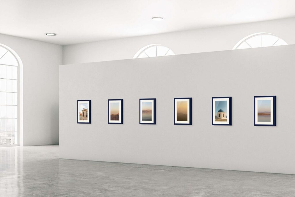 Six framed photographs hung in a row on a white gallery wall with arched windows